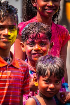 Children celebrating Holi with colorful face paint, smiling joyfully outdoors.