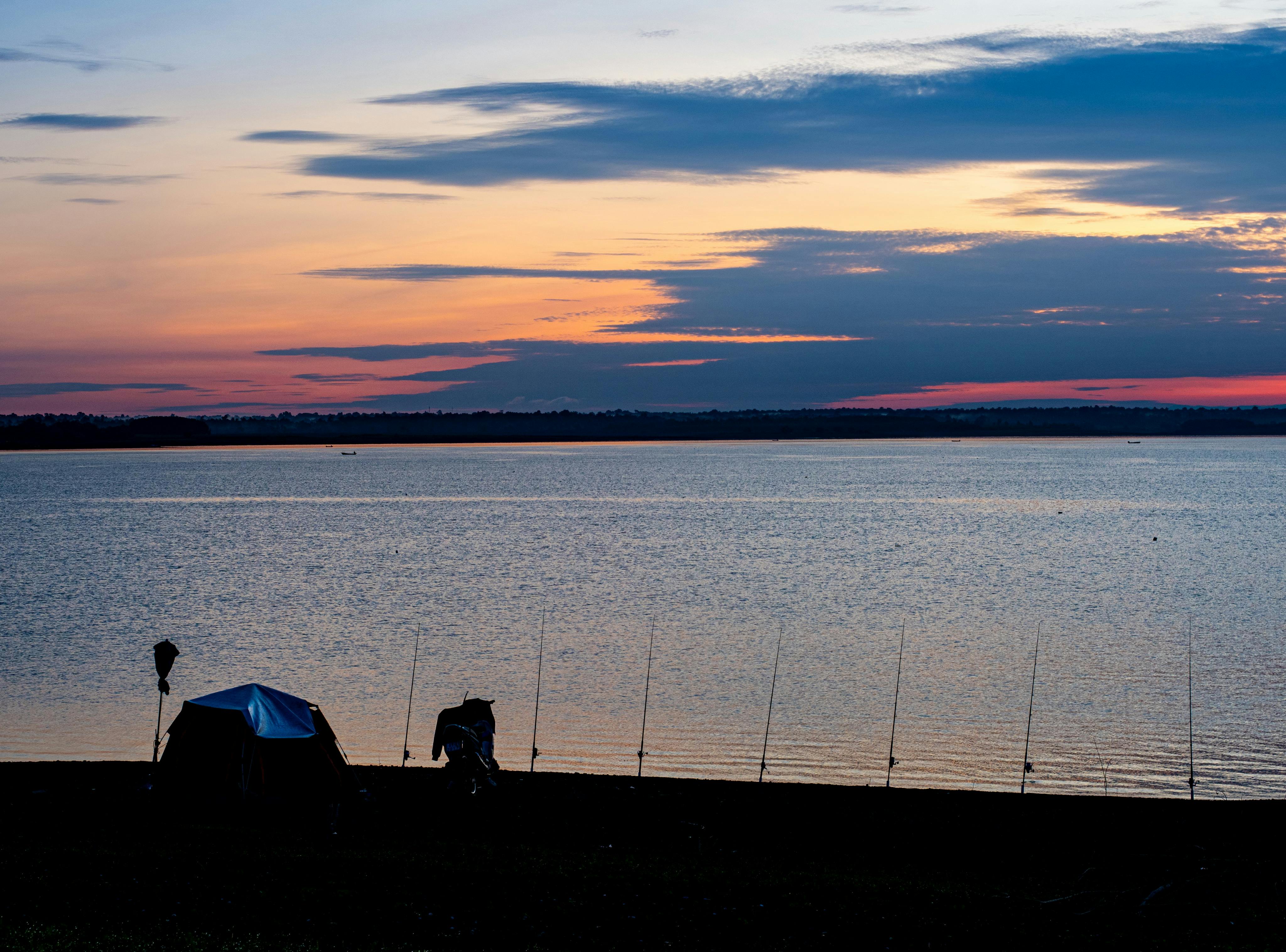 Tranquil lakeside view at sunset with a tent and fishing rods on the shore.