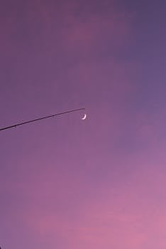 A crescent moon beside a rod at twilight against a vibrant purple sky, perfect for backgrounds.