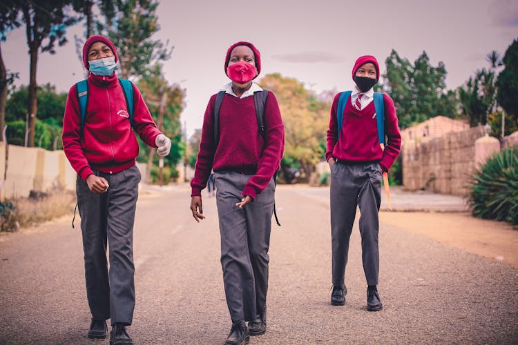 A Group Of Men In Uniform Wearing Face Masks Walking Together On Asphalt Road
