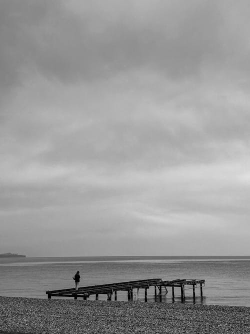 Free Grayscale Photo of a Person Standing on a Pier Stock Photo