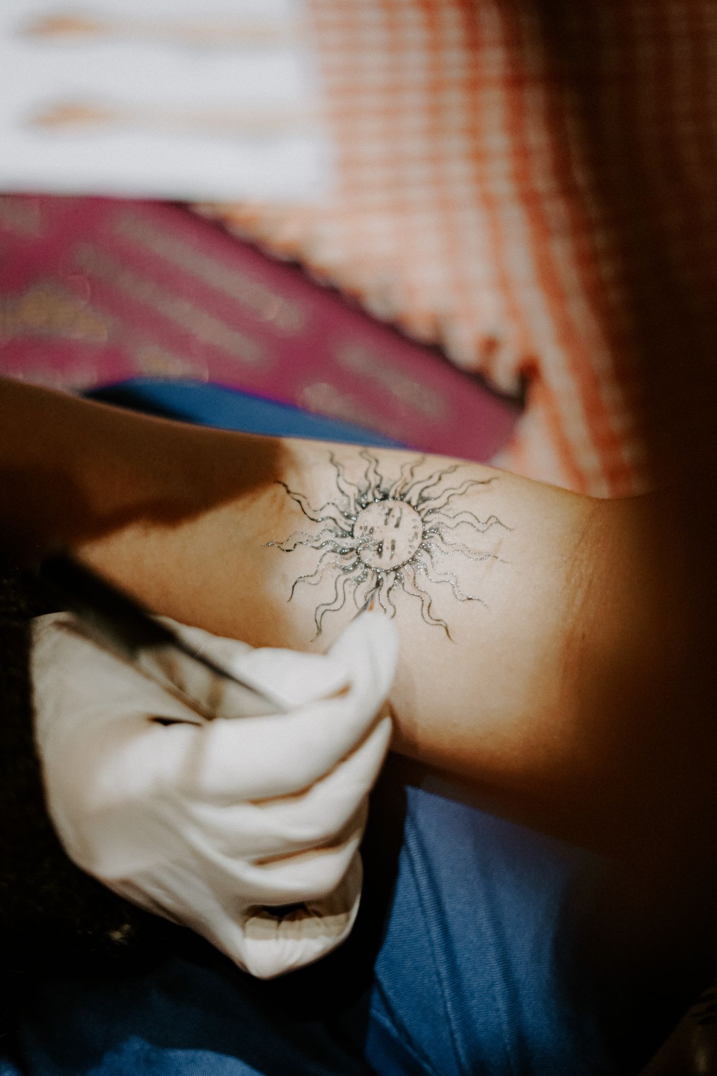 A small fine-line sun tattoo visible on an arm.