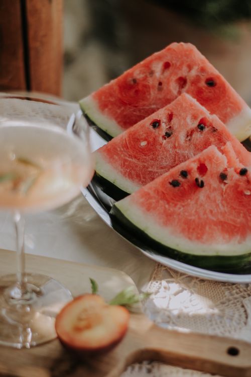 Free Close-up of fresh watermelon slices on a plate with a drink and peach, perfect for summer refreshment. Stock Photo