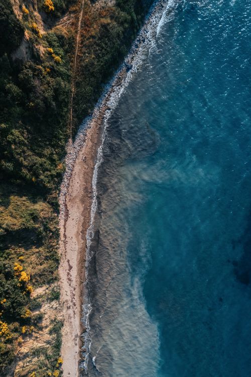 Free A stunning aerial view capturing the vibrant blue shoreline meeting green cliffs, showcasing nature's beauty. Stock Photo