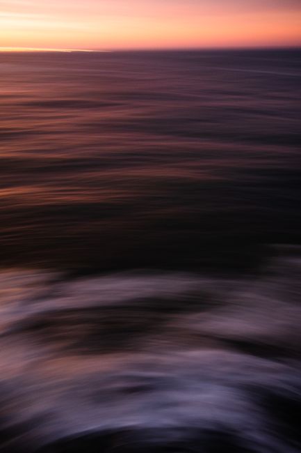 Abstract image of blurred ocean waves at sunset, showcasing vibrant colors and motion.