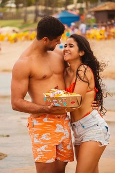 Happy couple embracing on a sunny beach, sharing a joyful moment and holding snacks.