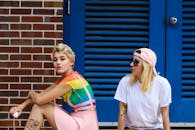 两位身着五颜六色服装的时尚人士，在充满活力的砖墙前摆姿势