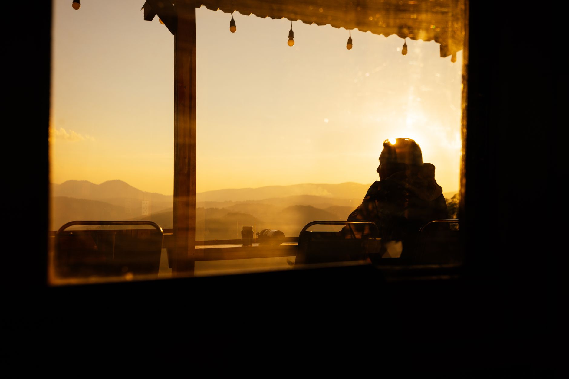 Captivating silhouette of a man through a window during a Dalat sunset, with scenic mountain views.