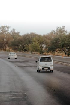 A quiet highway scene with two cars traveling under a clear sky, surrounded by trees.