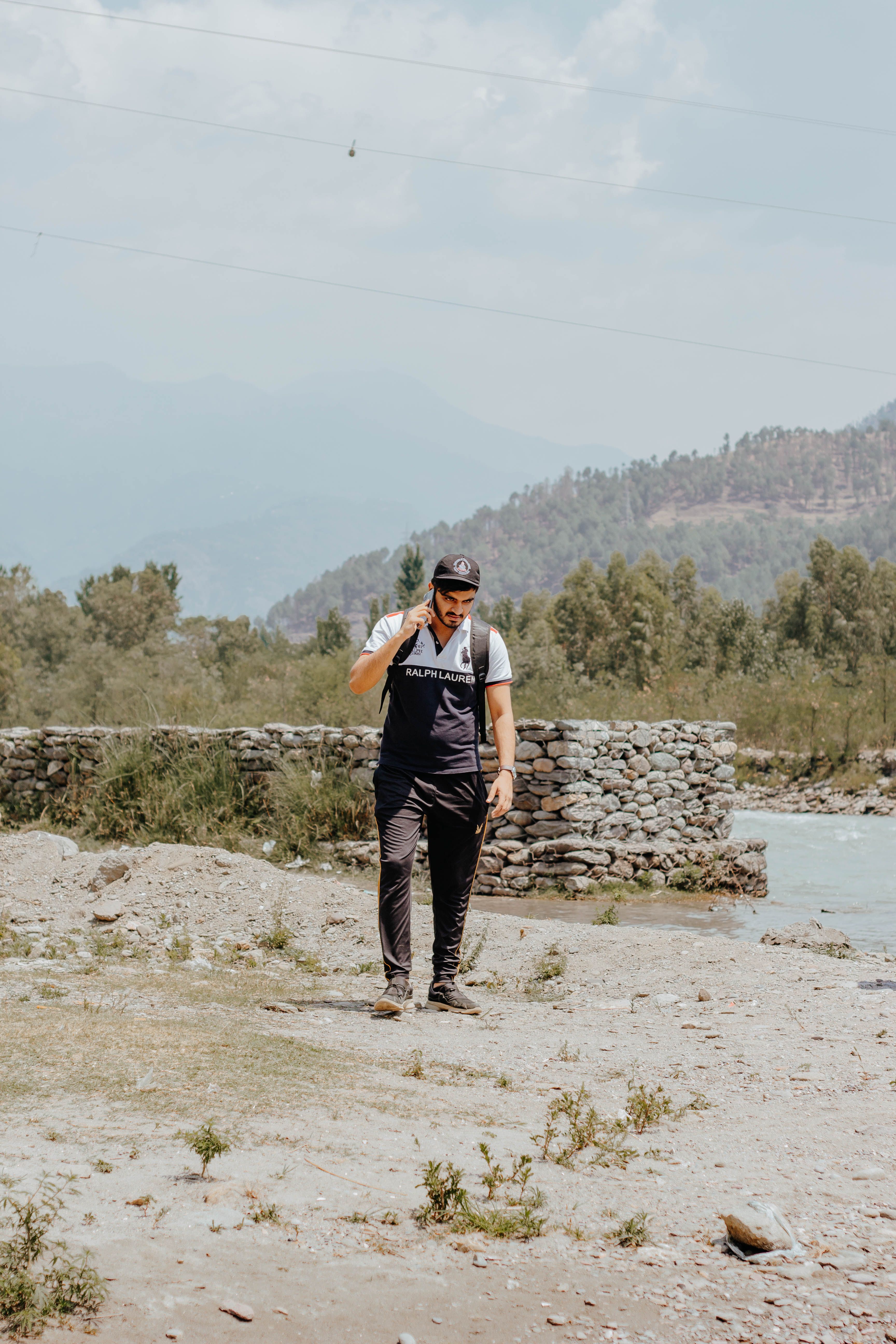 A man talking on his phone while walking in a scenic countryside with mountains in the background.