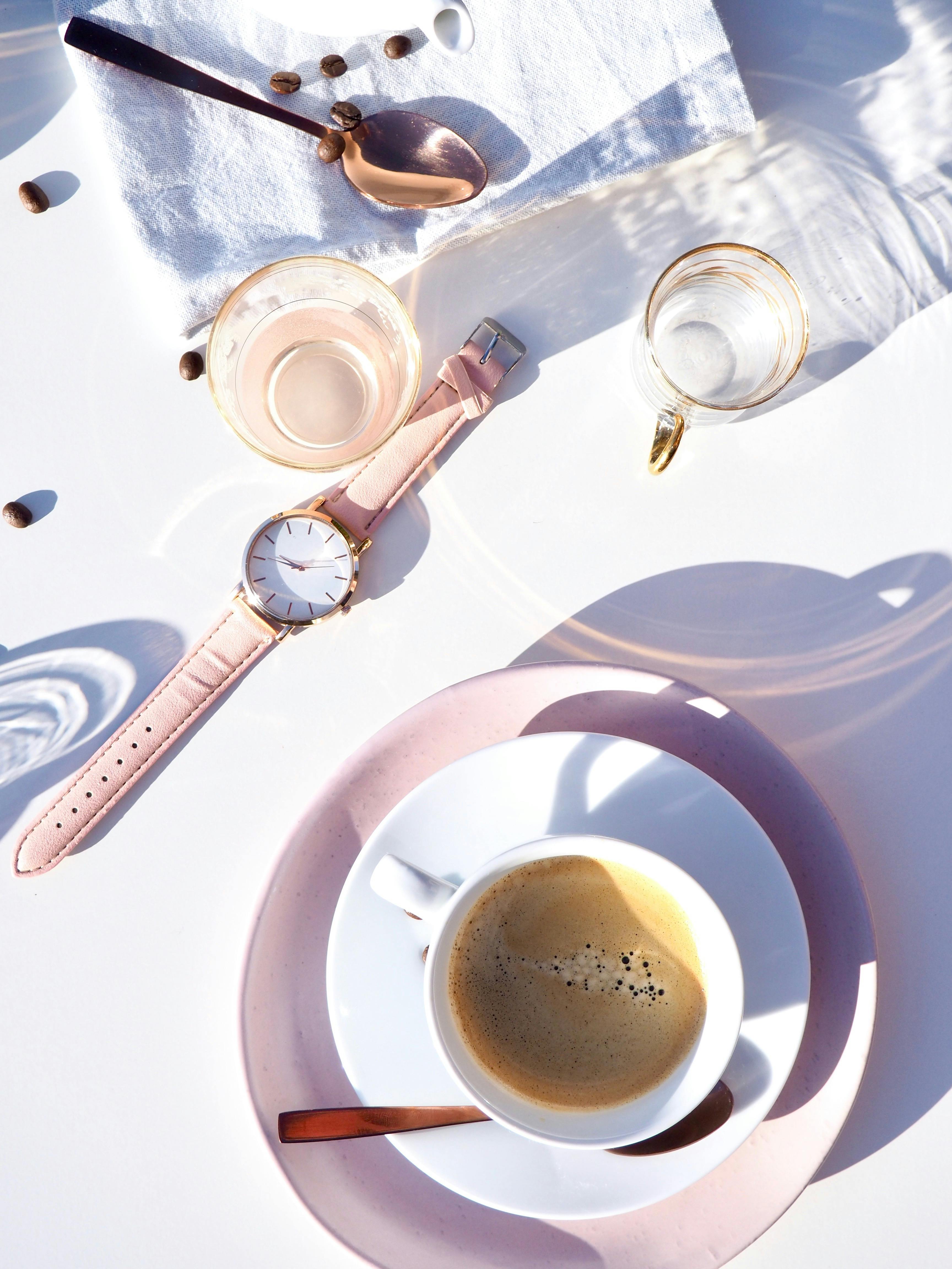 White Ceramic Cup on Saucer Near Gold-colored Analog Watch on Table