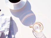 Empty glass reflecting sun near cup of coffee in morning