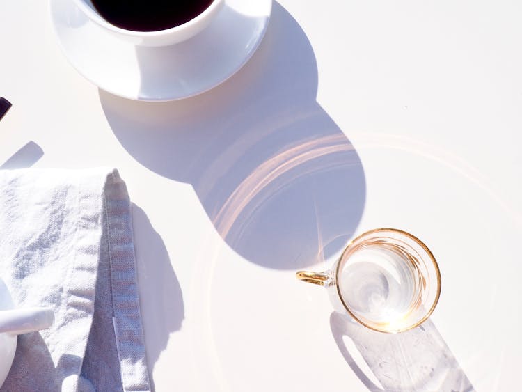 Empty Glass Reflecting Sun Near Cup Of Coffee In Morning