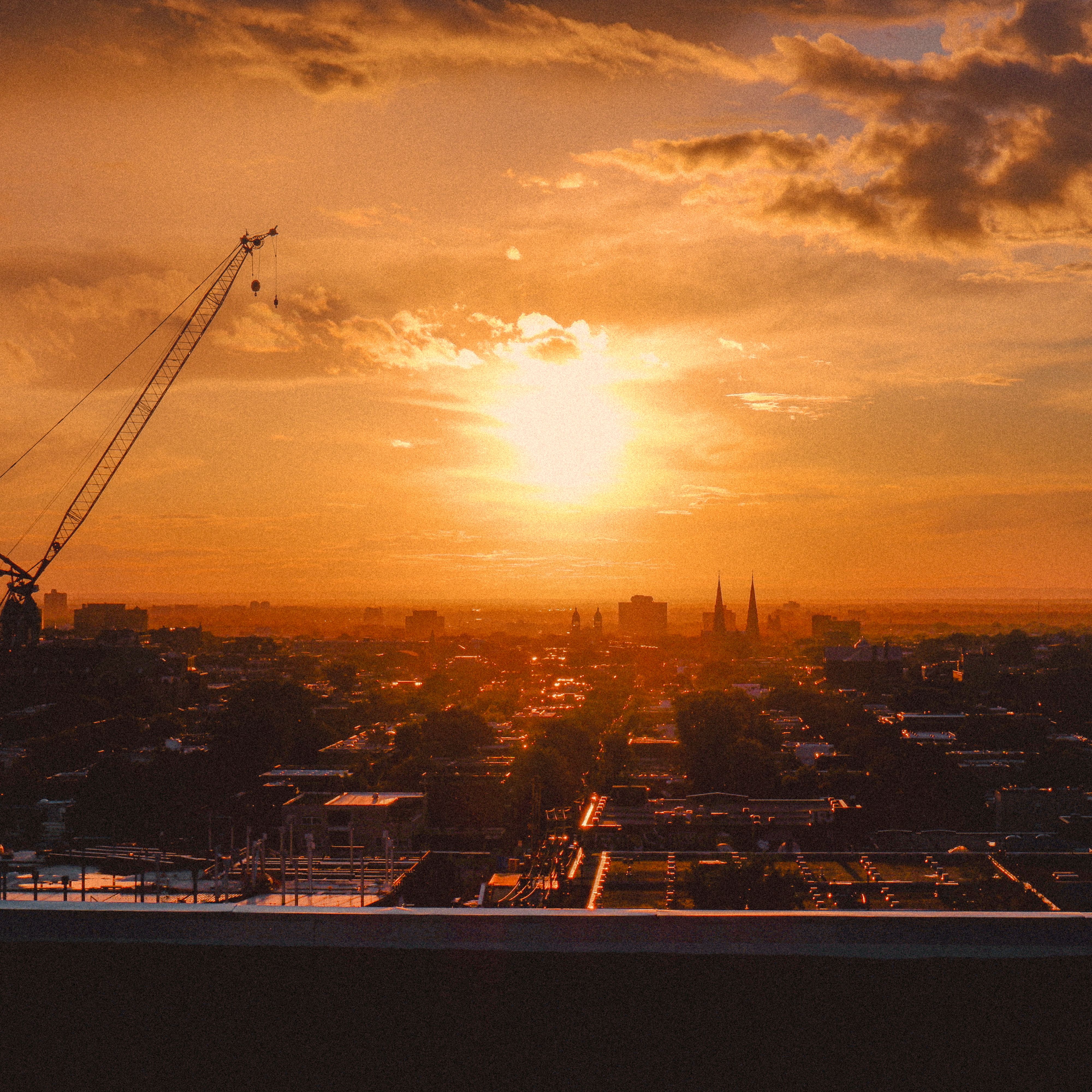Silhouette of a city skyline at sunset featuring a construction crane and dramatic clouds.