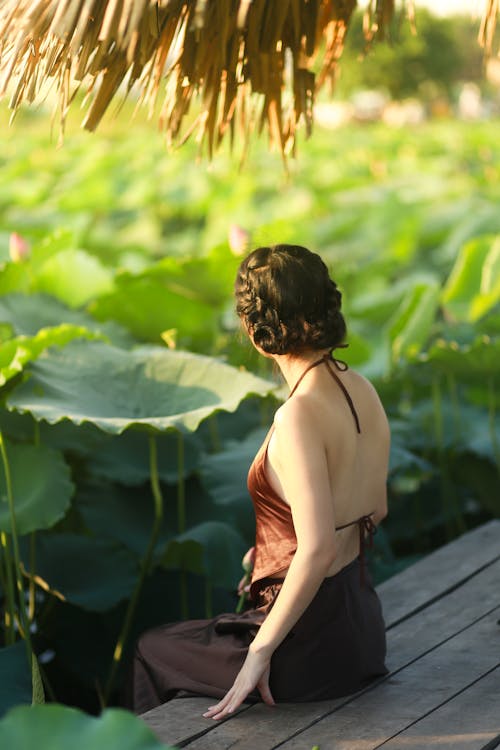 Woman in Brown Sexy Top Sitting on a Wooden Dock Near Green Plants