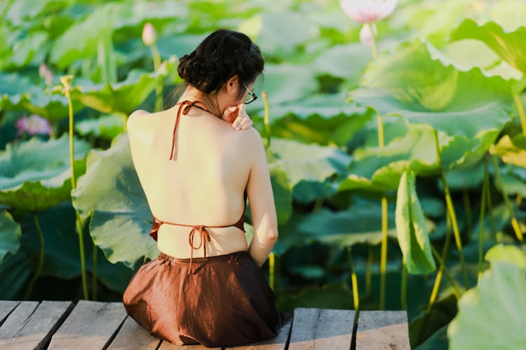 Woman In Brown Backless Double Tie Top Sitting On Wooden Deck Near Plants