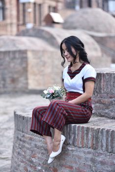 Charming woman with bouquet sitting on stone steps, showcasing fashion and grace. — photo by Lily Beth