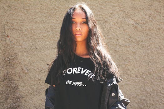 Portrait of a young woman with long hair posing against a textured wall, wearing a black t-shirt in sunlight.