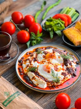 Turkish poached eggs with spicy tomato sauce, surrounded by fresh vegetables and bread.