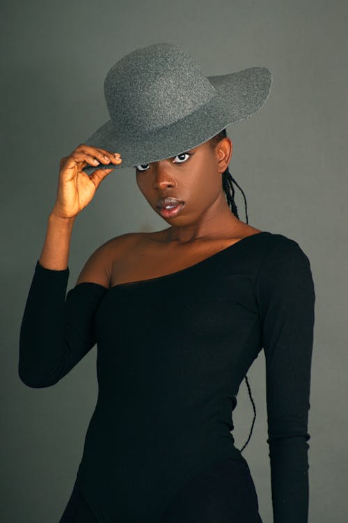 Close-Up Shot of a Woman in Black Long Sleeves Wearing Her Gray Hat on Gray Background