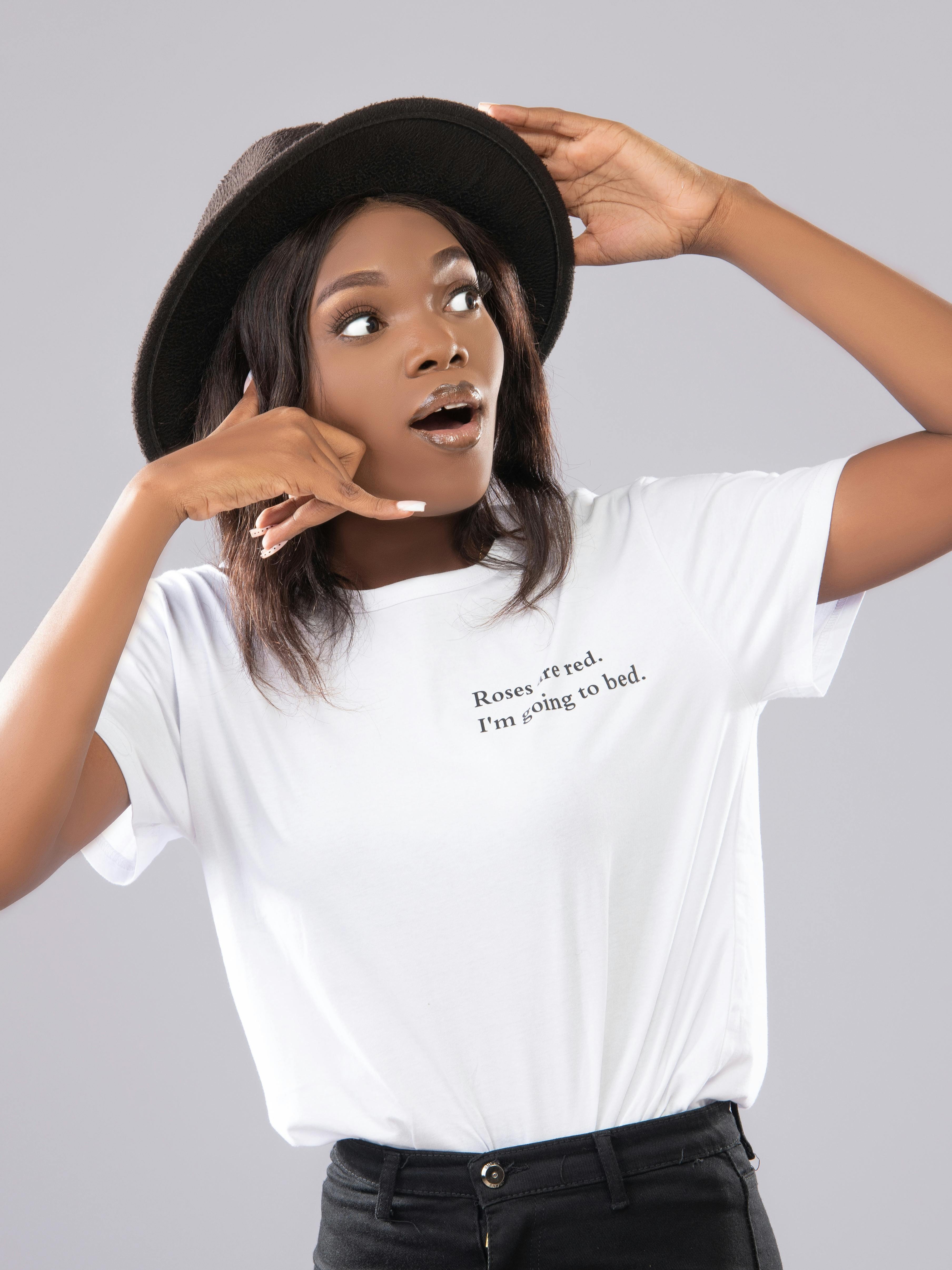 A surprised woman with a hat making a hand gesture in a playful manner against a white background.