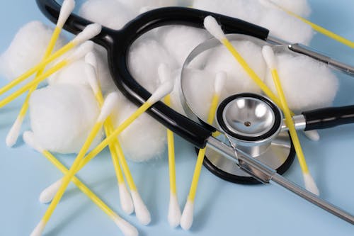 Stethoscope Beside Cotton Buds and Cotton Balls on a Blue Surface