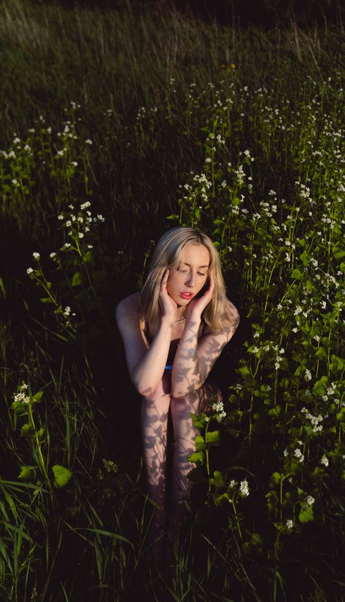 Free Blonde woman sitting among flowers in Toronto field during sunset, embodying tranquility and natural beauty. Stock Photo