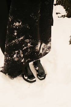 Close-up of black boots and long skirt on snow-covered ground.