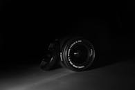 一张黑白照片捕捉了带帽数码单反相机镜头的细节，背景氛围戏剧性而阴郁