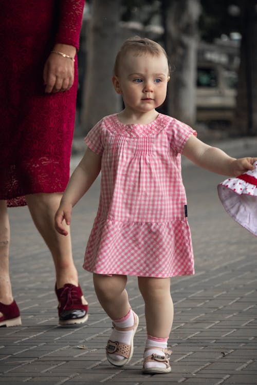 A Cute Toddler in Pink Dress Walking Beside a Woman in Red Dress