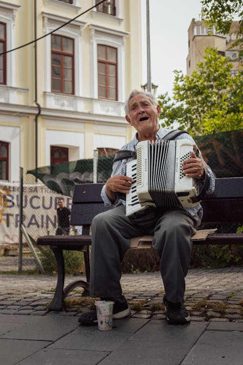 An Elderly Man Sitting on a Wooden Bench while Playing Accordion