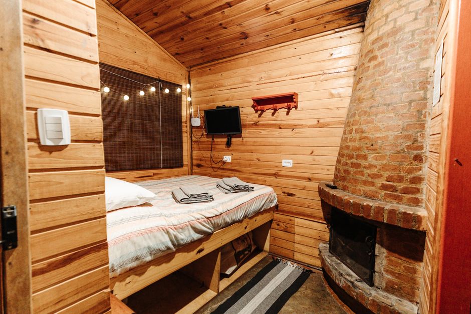 Warm wooden cabin bedroom featuring a rustic bed frame and brick fireplace, creating a cozy atmosphere.