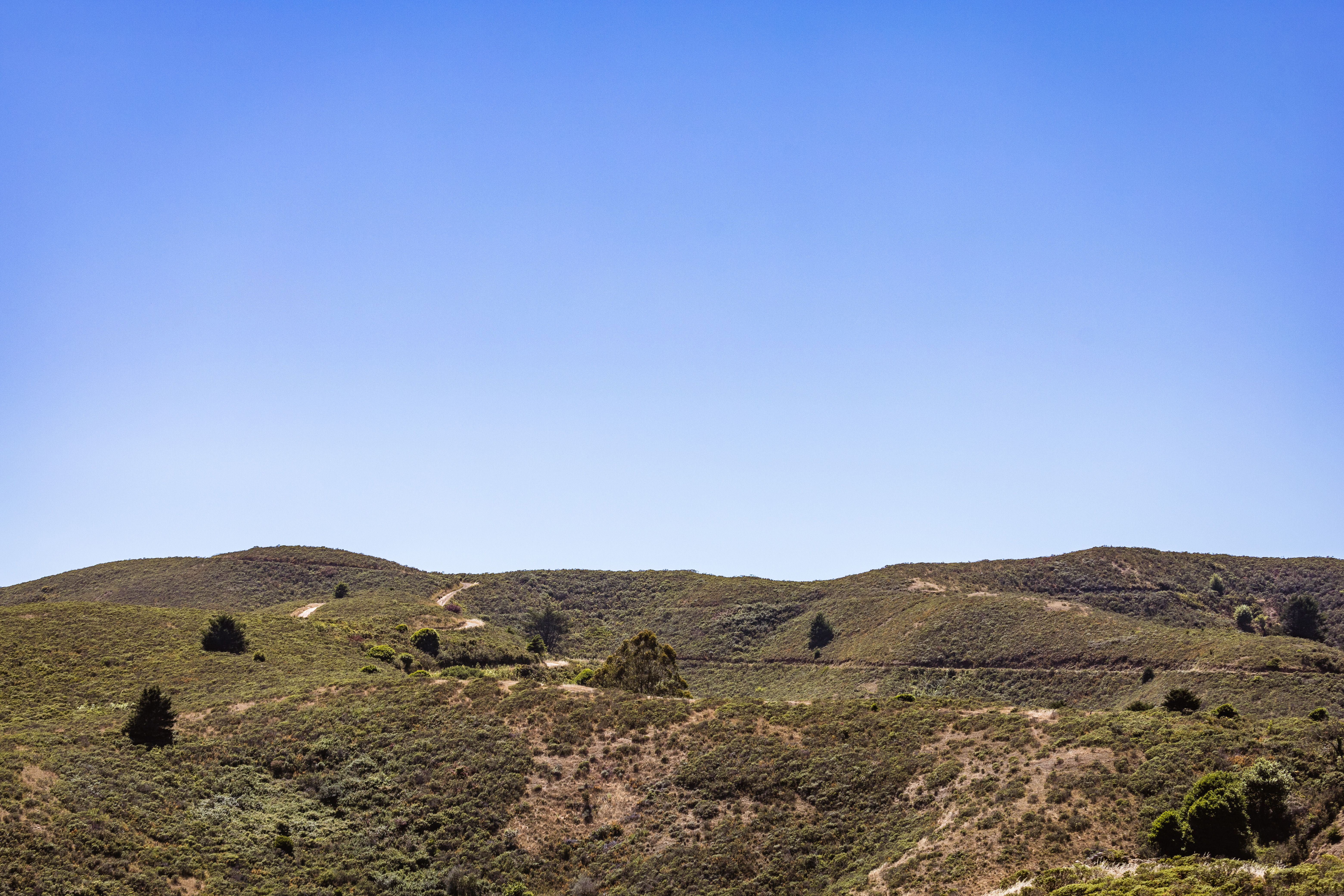 A serene landscape showcasing rolling green hills beneath a bright blue sky, perfect for nature lovers.