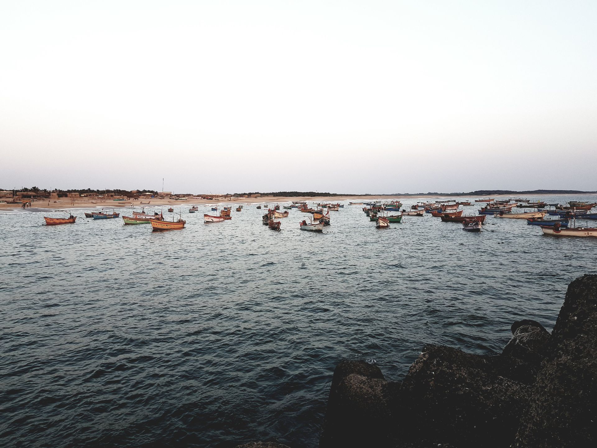 A serene view of wooden boats floating on the sea with a clear white sky in Junagadh, India.