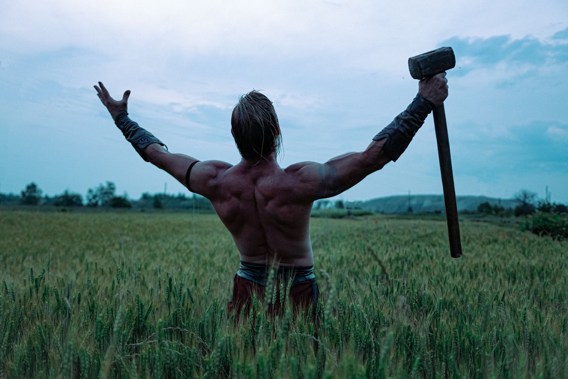 A strong shirtless man raising a hammer in a wheat field in Ukraine.