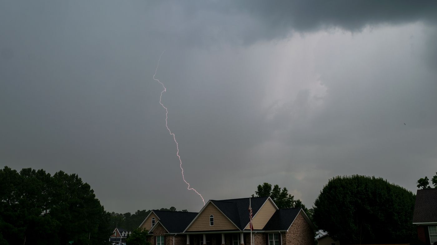 Lightning striking behind an intact home under a dark storm sky as hurricane season approaches