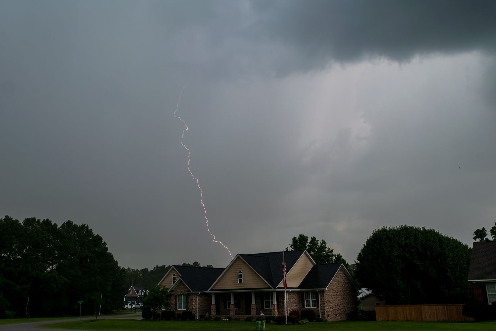 Lightning strikes behind a brick ranch home with an asphalt shingle roof as a thunderstorm moves over a Tennessee neighborhood