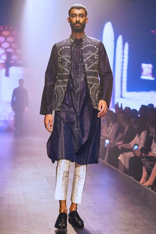 Free A male model wearing traditional attire walks confidently on a fashion runway. Stock Photo