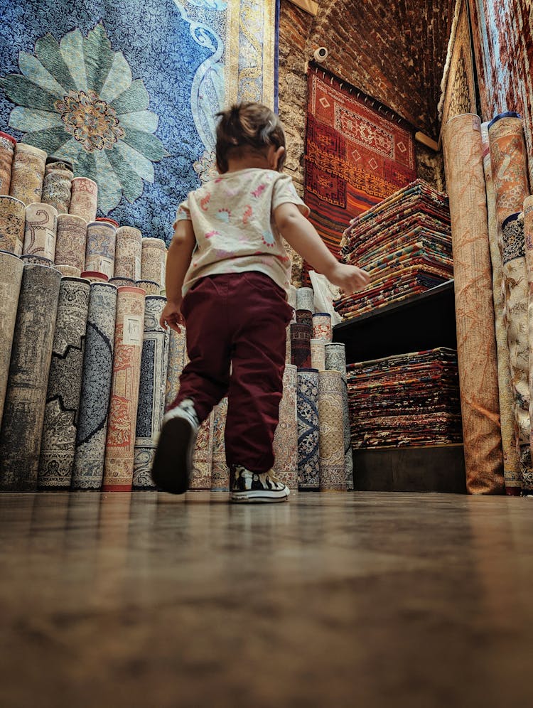 A Toddler Walking On The Floor Near Rolled Rugs 