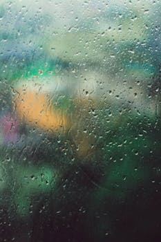 Water droplets on a glass window with a blurred outdoor landscape in the background.