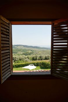 View of lush green fields and hills through an open wooden window in Kaymakoba, Turkey.
