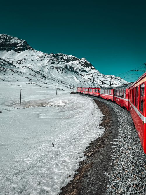 Free A red train travels through snow-covered mountains in the Swiss Alps under a bright blue sky. Stock Photo