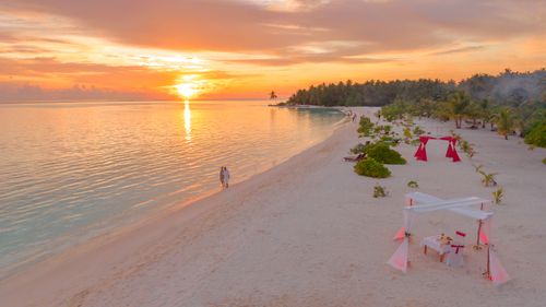 Free Couple enjoys a romantic walk on a serene Maldivian beach during a breathtaking sunset. Stock Photo