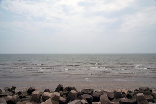 Free Calm ocean waves meet a rocky shoreline under a cloudy sky. Stock Photo