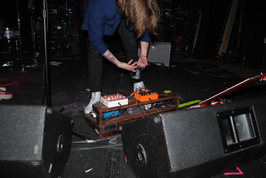 Musician adjusting audio equipment on stage during live performance, showcasing setup skills and technology.