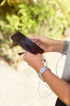 Close-up of hands holding a smartphone with earphones outdoors, showcasing modern technology.