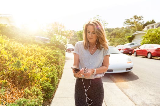 Woman walking outdoors with earphones, using a smartphone, enjoying a sunny day.