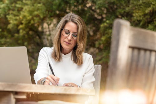 Woman Sitting on Gray Chair While Writing on Table