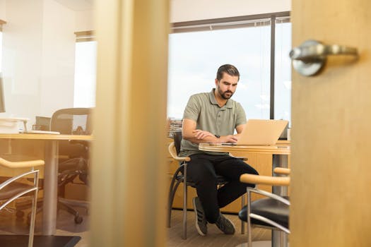 Professional man sitting at desk in modern office, working on laptop.