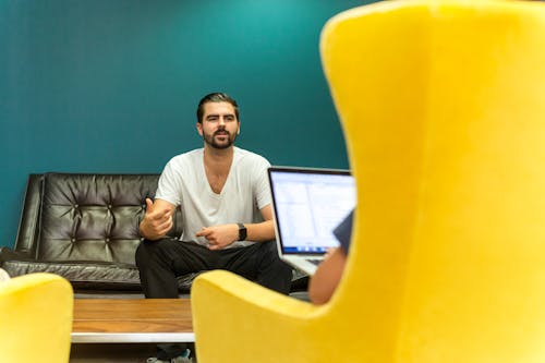 Man Sitting on Couch in Front of a Person Using a Laptop Computer